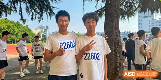 Two male students wearing matching racing bibs smile together while posing for a photo on the school campus at XuZhou No.3 Middle School.