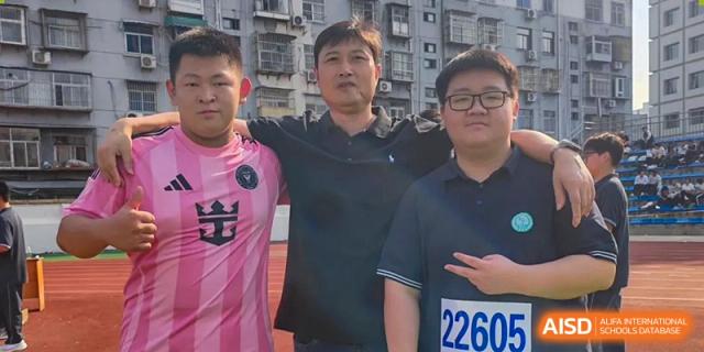 A teacher stands with his arms around two students on the athletic field, all smiling for a commemorative photo at XuZhou No.3 Middle School.