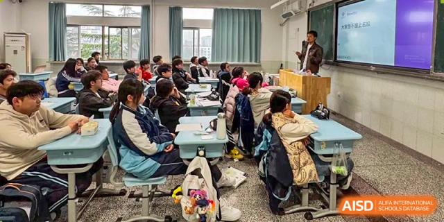 Students are seated at light blue desks in a tidy classroom while participating in a group learning activity at XuZhou No.3 Middle School.