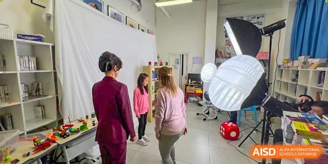 A teacher in a pink jacket talks with a young student in a school hallway near photography studio umbrellas at École Française Internationale de Canton(EFIC)