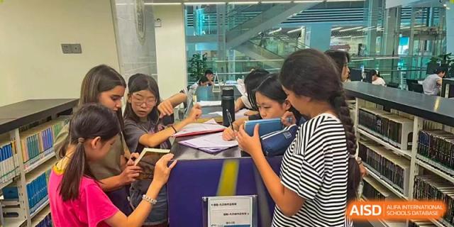 Students gather around a desk in a library to look at documents or school projects together during a lesson at École Française Internationale de Canton(EFIC)