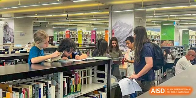 Students collaborate on a group project in a school library while standing near white bookshelves at École Française Internationale de Canton(EFIC)