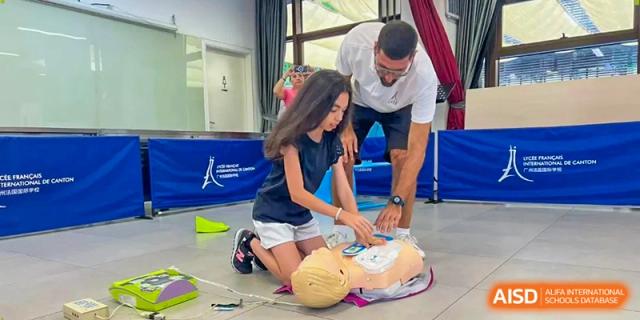 An instructor guides a student through a first aid training session using a medical mannequin on a blue mat at École Française Internationale de Canton(EFIC)