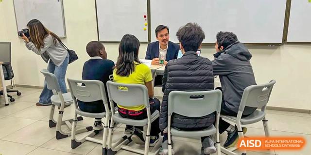 A teacher sits at a desk while conducting a small group discussion with students in a bright classroom at École Française Internationale de Canton(EFIC)