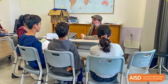 A teacher wearing a cap talks with students in a classroom featuring a large world map on the back wall at École Française Internationale de Canton(EFIC)