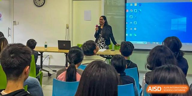 A teacher stands at the front of a room and speaks to a group of students during a school seminar or talk at École Française Internationale de Canton(EFIC)