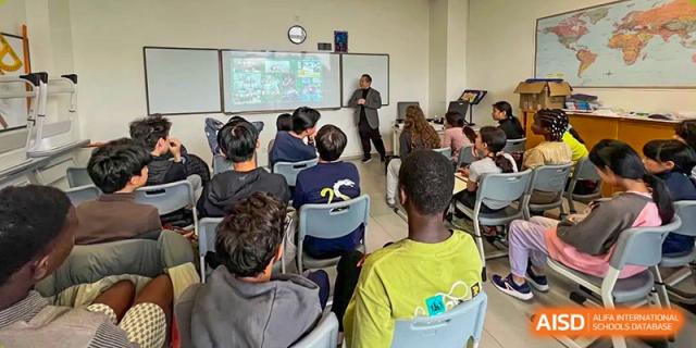 Students sit in a classroom and watch a teacher give a presentation using an interactive whiteboard at École Française Internationale de Canton(EFIC)