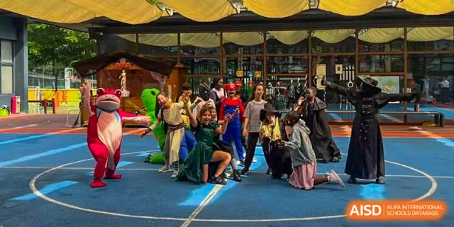 A group of children in various costumes, including a superhero and an explorer, pose together on a blue mat at École Française Internationale de Canton(EFIC)