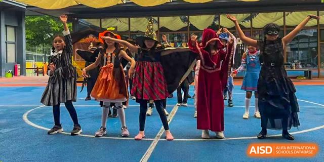 Three young students in colorful costumes perform a dance on a blue indoor court during a school celebration at École Française Internationale de Canton(EFIC)