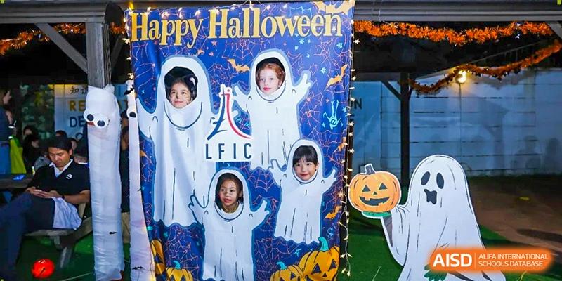 Children pose behind a decorative Halloween photo board featuring ghost cutouts and pumpkins at École Française Internationale de Canton(EFIC)