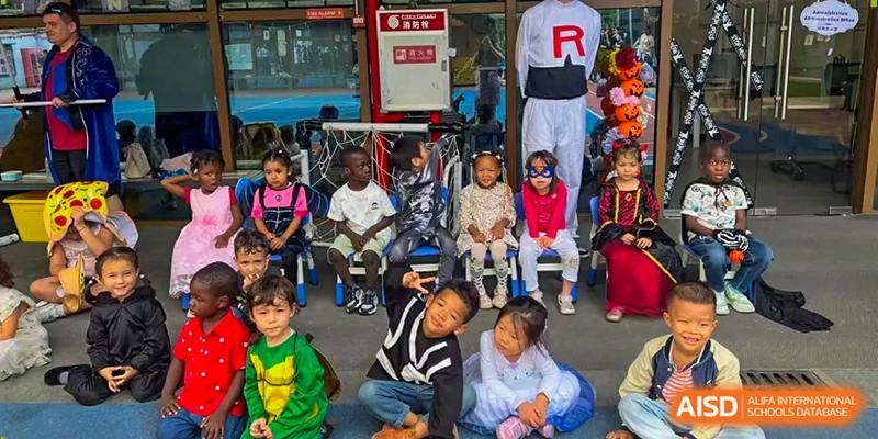 Young students in diverse costumes sit in a row and smile for a group photo during a festive school event at École Française Internationale de Canton(EFIC)