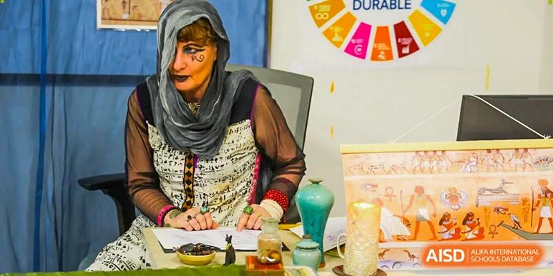 A woman in a patterned headscarf and costume works at a table with small decorative items during a school fair at École Française Internationale de Canton(EFIC)