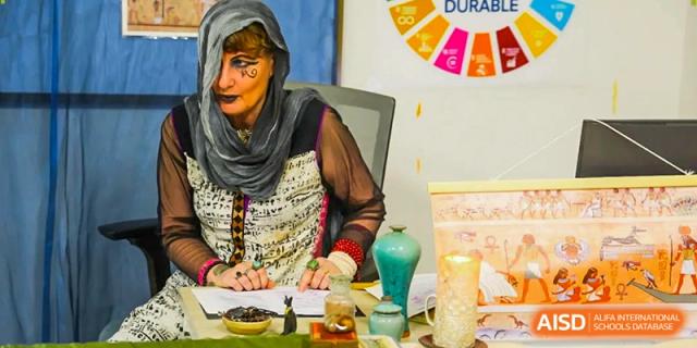 A woman in a patterned headscarf and costume works at a table with small decorative items during a school fair at École Française Internationale de Canton(EFIC)