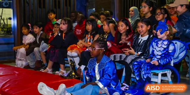 A group of students in vibrant costumes watch a performance from their seats in a darkened auditorium at École Française Internationale de Canton(EFIC)