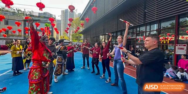 Students and staff participate in a rhythmic stick activity outdoors on a blue court during a cultural event at École Française Internationale de Canton(EFIC)