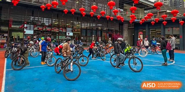 Students ride their bicycles across a blue outdoor court decorated with hanging red lanterns at École Française Internationale de Canton(EFIC)