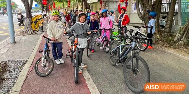 A group of students wearing helmets and casual clothing prepare for a bicycle ride together on a paved path at École Française Internationale de Canton(EFIC)