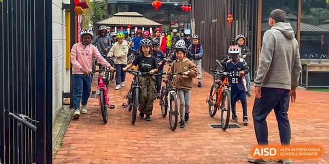 A large group of young students wearing bicycle helmets and backpacks prepares for a group ride outdoors at École Française Internationale de Canton(EFIC)
