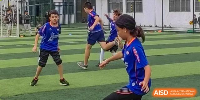 Two young soccer players in blue uniforms compete for the ball during an active match on a green turf field at École Française Internationale de Canton(EFIC)