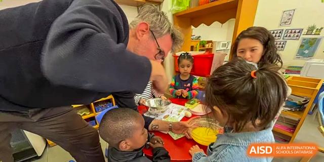 A teacher assists young students with a hands-on cooking activity involving eggs and mixing bowls in a classroom at École Française Internationale de Canton(EFIC)