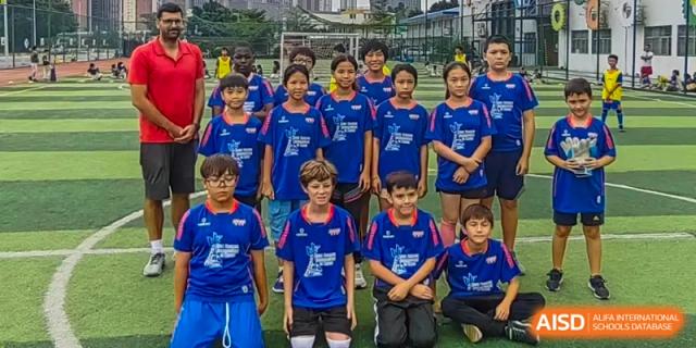 A large team of young soccer players in matching blue and red uniforms pose together on an outdoor field at École Française Internationale de Canton(EFIC)