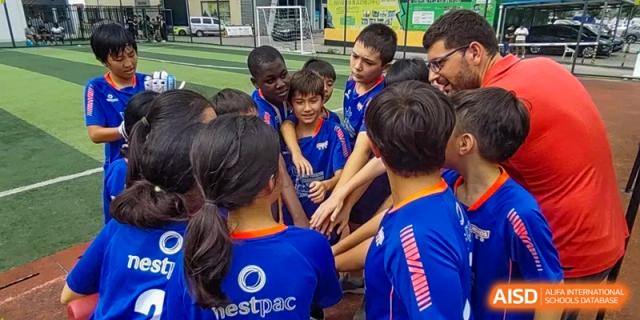 A group of students in blue athletic wear huddle together and place their hands in the center for a team cheer at École Française Internationale de Canton(EFIC)
