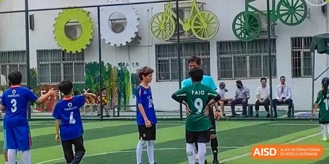 A young student in a blue jersey stands on a soccer field while a coach in a green shirt observes at École Française Internationale de Canton(EFIC)