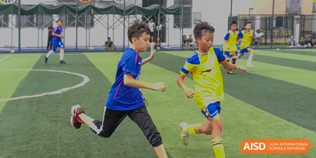A young boy in a blue athletic shirt runs across a green soccer pitch during a school sports event at École Française Internationale de Canton(EFIC)