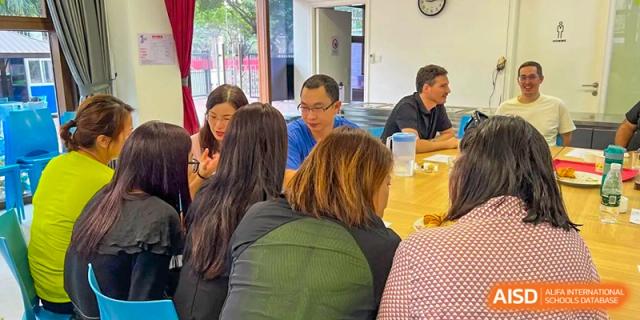 Adults sit at a long wooden table during a collaborative school meeting or workshop in a bright room at École Française Internationale de Canton(EFIC)