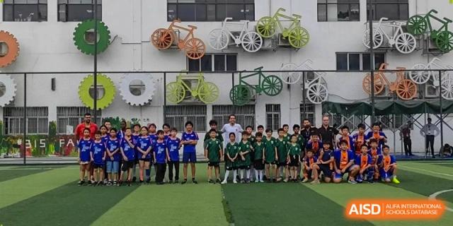 A group of young students in green and blue athletic uniforms pose for a team photo in front of a decorated wall at École Française Internationale de Canton(EFIC)