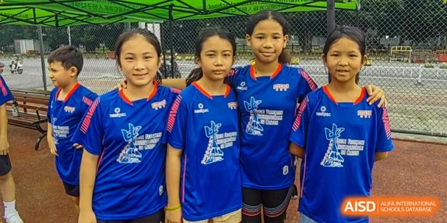Three young female students in blue and red athletic uniforms stand together and smile on a soccer field at École Française Internationale de Canton(EFIC)