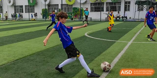 A young boy in a blue soccer uniform prepares to kick a ball on an outdoor green turf field at École Française Internationale de Canton(EFIC)