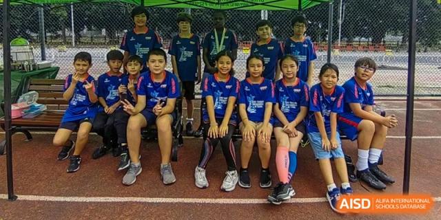 A team of young students wearing blue and red jerseys sit together on a red track for a group photo at École Française Internationale de Canton(EFIC)