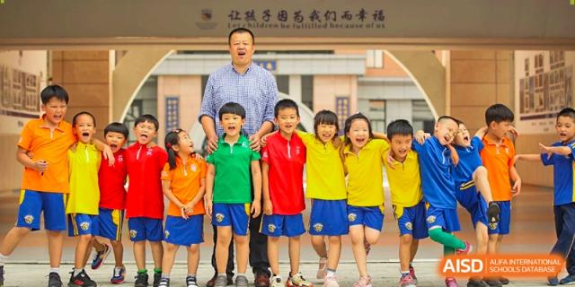 A teacher stands with a group of smiling students in vibrant red, green, and yellow shirts at Beijing International Bilingual Academy Guiyang.