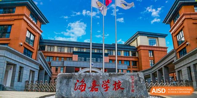 The school's main building stands tall under a blue sky with flags flying at the entrance of Beijing International Bilingual Academy Guiyang.
