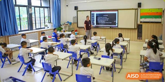 Students sit at white desks in a modern, bright classroom while a teacher leads a lesson at Beijing International Bilingual Academy Guiyang.