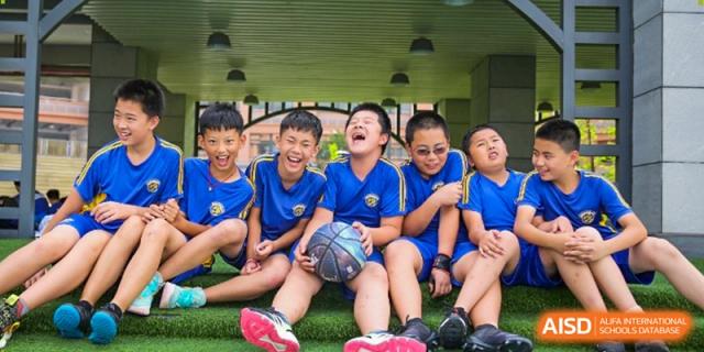 A group of young boys in blue jerseys sit together laughing while holding a basketball at Beijing International Bilingual Academy Guiyang.