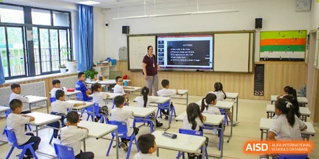 A wide view of a classroom shows students engaged in a digital lesson projected on a smart board at Beijing International Bilingual Academy Guiyang.