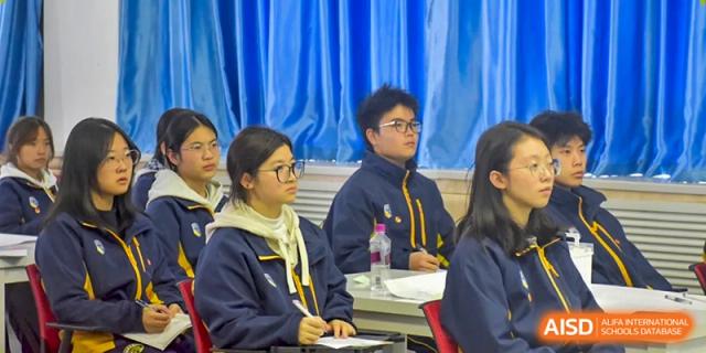 Two older students in dark school blazers sit at their desks during a focused classroom discussion at Beijing International Bilingual Academy Guiyang.