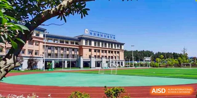 An expansive view shows the multi-story school building and the red running track on a sunny day at Beijing International Bilingual Academy Guiyang.