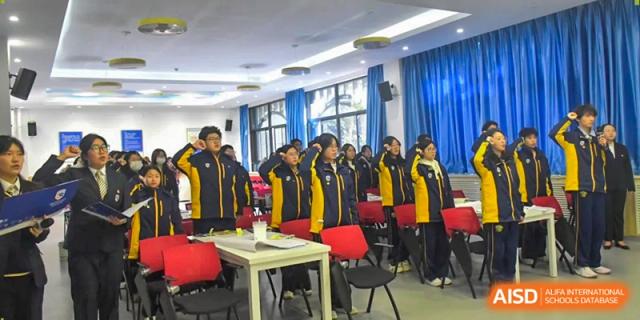 Students in yellow and black tracksuits stand together in a classroom during a group activity at Beijing International Bilingual Academy Guiyang.