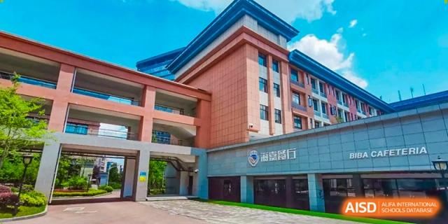 A modern red brick school building with multiple stories and large windows under a clear blue sky at Beijing International Bilingual Academy Guiyang.
