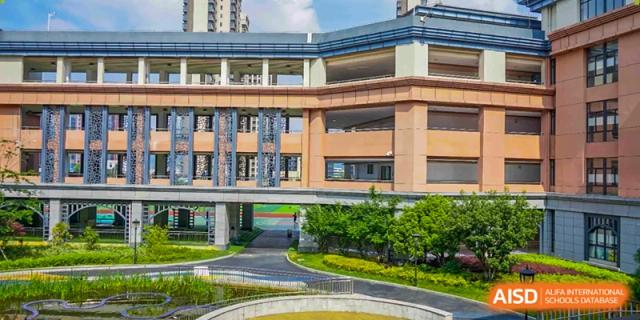 An elevated walkway connects two wings of the modern brick campus surrounded by lush greenery at Beijing International Bilingual Academy Guiyang.