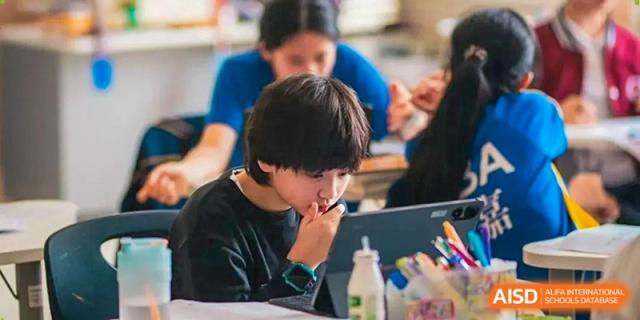 A young student focuses intently on his schoolwork while sitting at a desk in a bright classroom at Beijing International Bilingual Academy Guiyang.