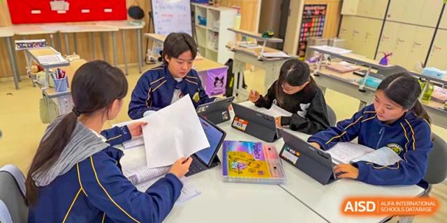 Students collaborate in a group, looking at papers and tablets during an interactive class at Beijing International Bilingual Academy Guiyang.