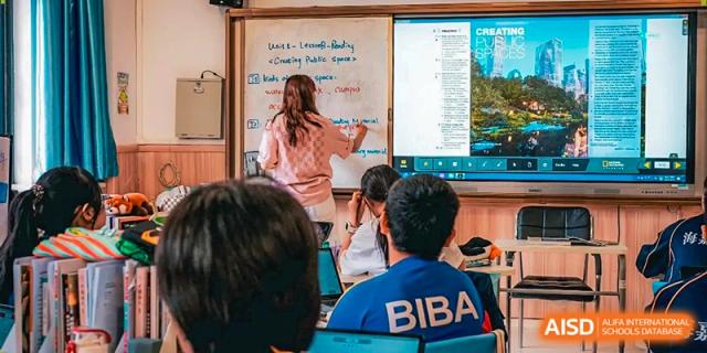 A teacher stands at a whiteboard while students in blue uniforms follow along with the lesson at Beijing International Bilingual Academy Guiyang.