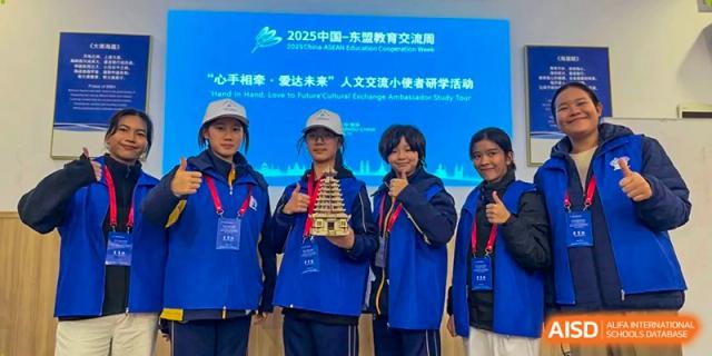 Three students in blue athletic jackets smile and hold up a model they built for a project at Beijing International Bilingual Academy Guiyang.
