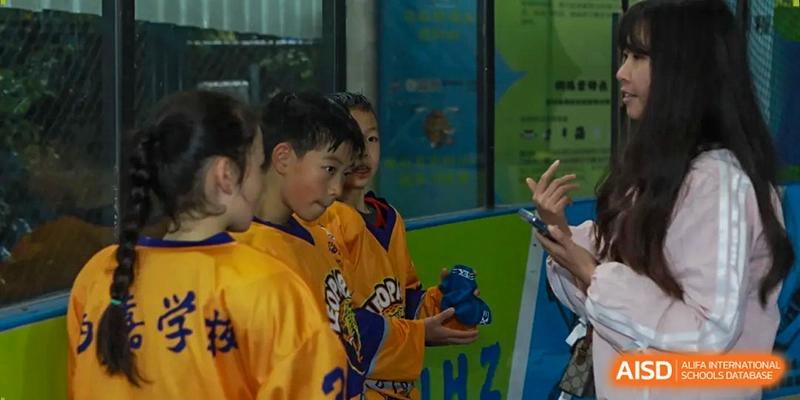 Students in yellow and purple sports jerseys gather for a team briefing during a hockey event at Beijing International Bilingual Academy Guiyang.