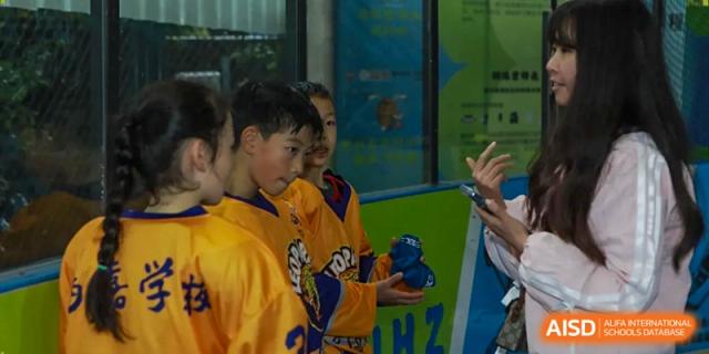 Students in yellow and purple sports jerseys gather for a team briefing during a hockey event at Beijing International Bilingual Academy Guiyang.