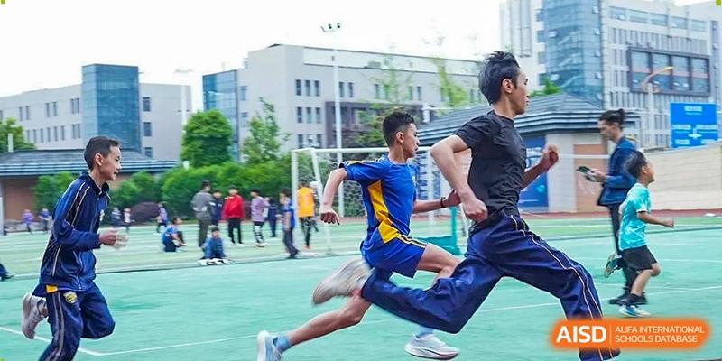 A student in a blue athletic kit sprints across a green sports field during a competitive track event at Beijing International Bilingual Academy Guiyang.